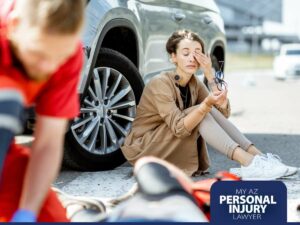Injured woman sitting by a damaged car after a traffic accident as paramedics provide assistance – My AZ Personal Injury Lawyer