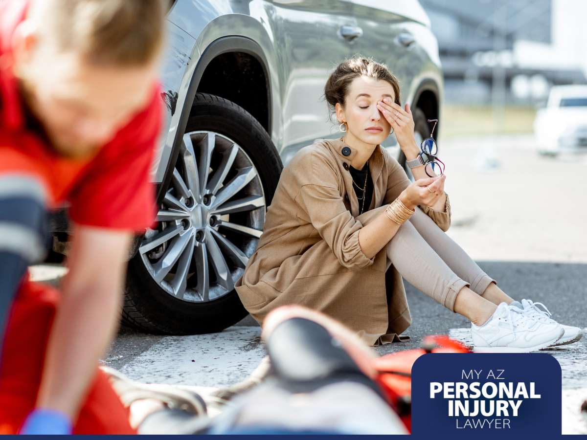 Injured woman sitting by a damaged car after a traffic accident as paramedics provide assistance – My AZ Personal Injury Lawyer